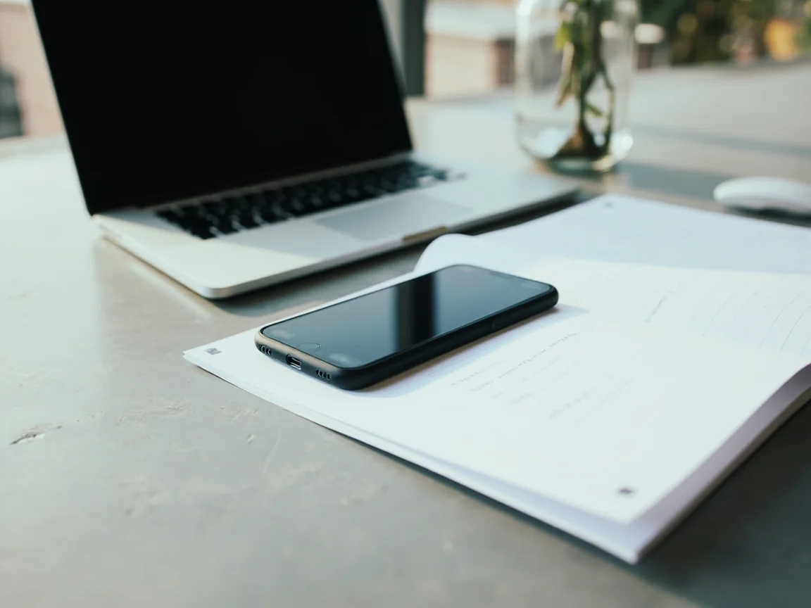 Editorial photograph of a writer's desk during a rummy platform review, a matte laptop open with the screen turned away from the camera