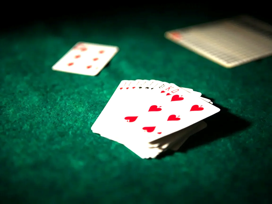 Editorial photograph of a folded rummy hand of approximately twelve cards resting on a green baize, a single open draw pile card beside it, a small card-counting chart in soft focus
